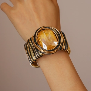 Detail of twisted wire cuff bracelet featuring a large yellow faceted gemstone centerpiece