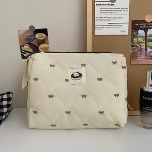 Close-up of quilted cream makeup bag featuring cartoon cat patch and embroidery
