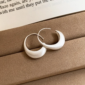 Detail view of silver crescent hoop earrings with brushed matte finish on a brown tray