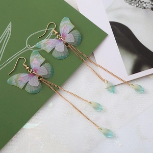 Détail de longues boucles d'oreilles dorées avec papillons colorés et gouttes d'eau
