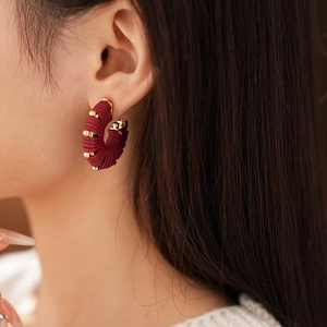 Detail of burgundy faux leather U-shaped striped earring worn by a model in a close-up view