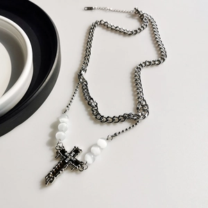 Detail of layered silver Cuban chain with white beads and cross pendant on white surface