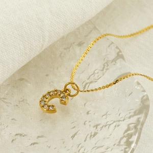 Detailed macro view of gold letter C pendant with sparkling pavé crystals on a fine chain
