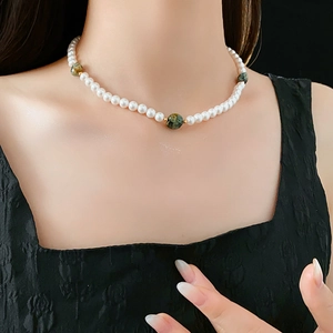 Gros plan du collier avec perles irrégulières et pierres vertes porté sur la clavicule