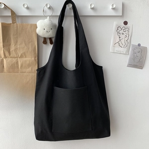 Detail of minimalist black canvas tote bag with large front pocket hanging on a wall hook