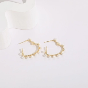Detailed close-up of hollow heart-shaped gold earrings adorned with white pearls
