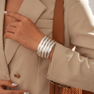 Gros plan sur un ensemble de cinq bracelets argentés martelés portés avec un blazer beige