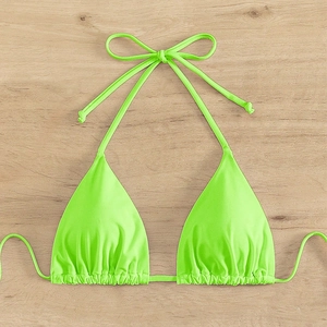 Detail of neon green halter bikini top with ruched triangle cups on wooden background