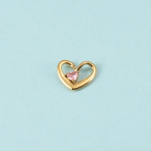 Macro d'un pendentif cœur doré avec pierre de naissance rose sur fond bleu clair