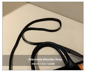 Detail view of the black handbag showing the cylindrical handle and adjustable strap