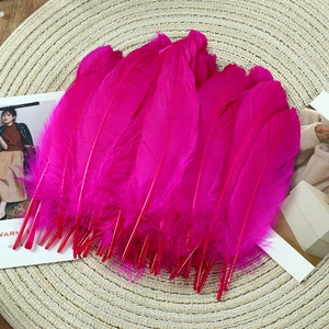 Vibrant rose red goose feathers for DIY crafts and wedding decor on woven mat