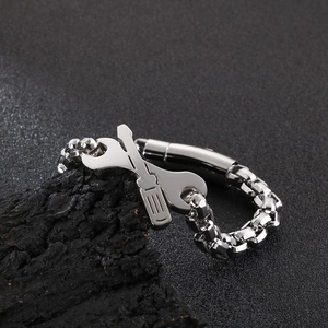 Detail of silver industrial bracelet with wrench and screwdriver charms on a dark surface