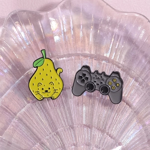 Cute enamel pins featuring yellow pear cat and grey gaming controller cat designs