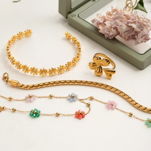 Flat lay of gold daisy bangle, flower ring, and beaded necklaces on a minimalist background