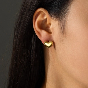Irregular gold heart stud earrings with milgrain edges worn by a female model