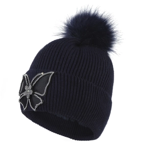 Women's dark blue knit beanie with a large faux fur pom and sparkling rhinestone butterfly