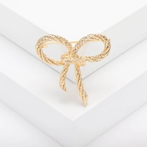 Elegant gold bow brooch with textured weave pattern displayed on a clean white stand