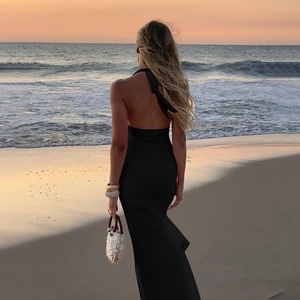 Robe longue dos nu à licou noire élégante présentée sur une plage au coucher du soleil