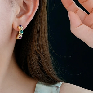 Close-up of vintage geometric gold hoop earrings with blue, green, and purple gemstones