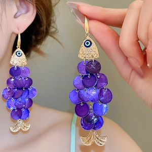 Detail of gold fish-shaped earrings with blue evil eye and purple sequins tassels