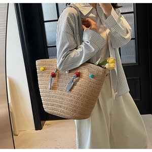 Detail of hand-woven tote bag with colorful pom-poms and tulip accents on model