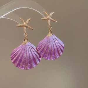 Detail view of gold starfish earrings with glossy purple shell pendants for beach wear