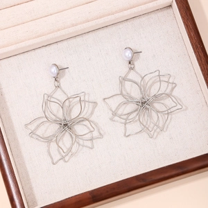 Fashionable layered silver woven flower earrings with white pearl accents on wood tray
