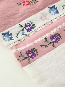Dettaglio ravvicinato del tessuto rosa e bianco con ricami floreali e bordo in pizzo