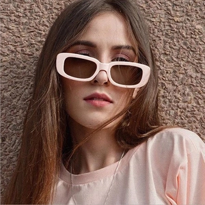 Close-up of retro rectangular beige sunglasses worn by a model against a stone wall