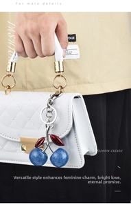 Detail of blue glitter cherry keychain charm hanging on a white quilted luxury handbag