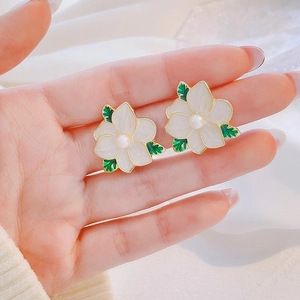Close-up of elegant white flower earrings with green leaves and a central pearl accent