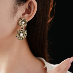 Close-up of golden vintage double flower earrings with pearls worn by a model