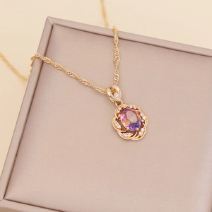 Detail of gold sunflower necklace with purple gradient stone on beige jewelry box