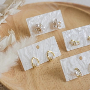 Minimalist pearl earrings and gold studs on marble display cards with wooden tray