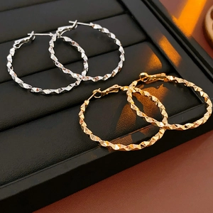 Dettaglio di orecchini a cerchio oro e argento con texture diamantata su display nero