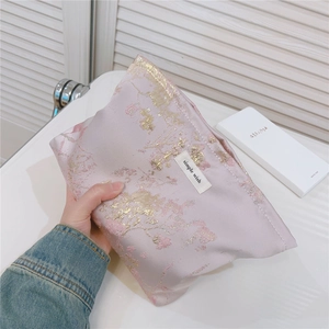 Détail du tissu jacquard floral sur une trousse de toilette rose avec étiquette