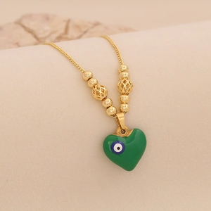 Détail d'une chaîne dorée avec pendentif cœur vert et motif œil maléfique