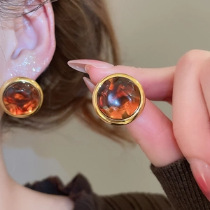 Close-up of vintage golden round earrings with amber resin texture on model ear