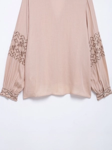 Detailed close-up of delicate floral embroidery on long-sleeved light pink cotton shirt