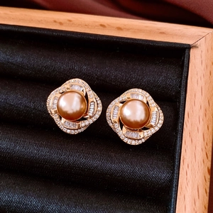 Close-up of luxury gold pearl stud earrings with zircon swirl detail on black velvet