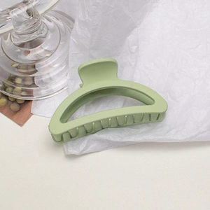 Close-up of a matte light green hollow claw clip on a textured white background