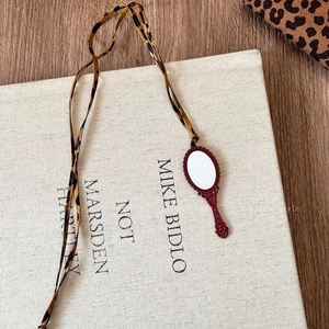 Detail view of leopard print ribbon necklace with vintage burgundy mirror pendant on book