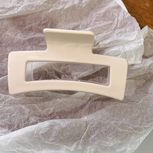 Detailed view of a cream rectangular hollow hair claw clip on white textured paper
