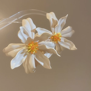 Close-up of oversized white acrylic flower earrings with yellow beaded centers