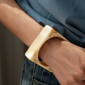 Close-up of a square acrylic bangle featuring cream and amber marble texture