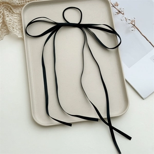 Detail of a black long ribbon bow hair tie on a beige frosted tray with lace and cotton