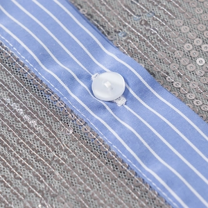 Vue détaillée du bouton blanc sur tissu à rayures bleues et paillettes argentées