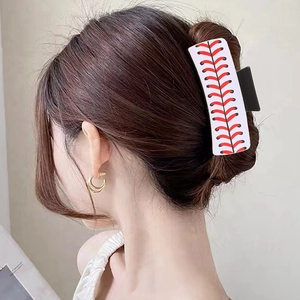 Detail shot of a white baseball-themed hair claw clip with red stitching on hair