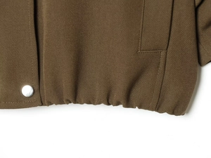 Close-up of olive green twill fabric featuring elastic hem and silver snap button detail