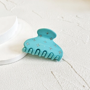 Detail of turquoise hair claw clip with sparkling crystal studs on a white surface